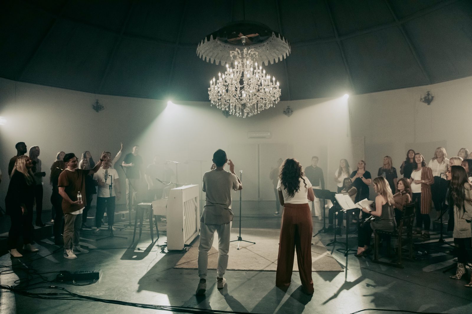 Robby and Bria Valderrama directing a choir under a chandelier